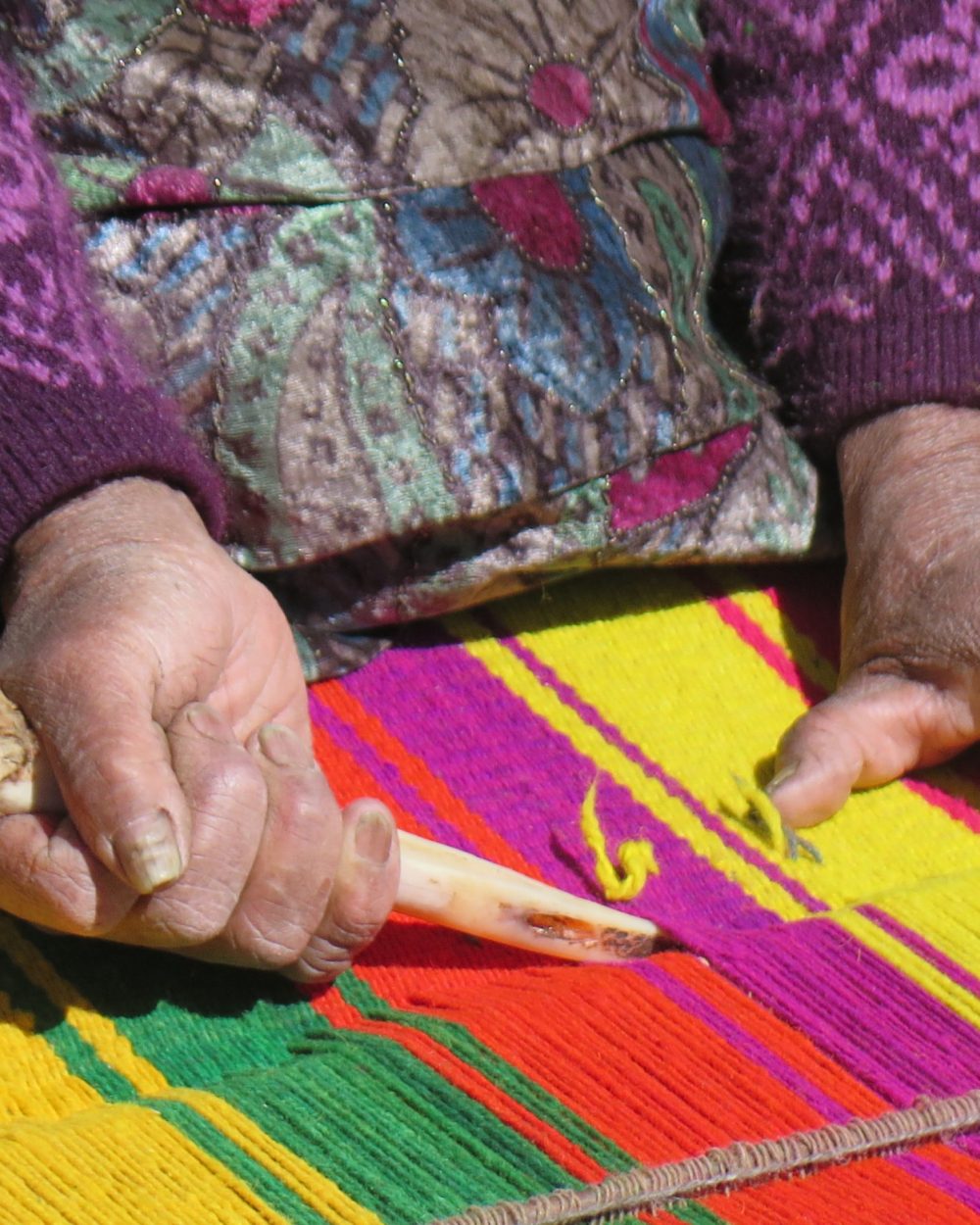 Mains d'une tisseuse aymara travaillant un tissage aux couleurs vives à Santiago de Okola